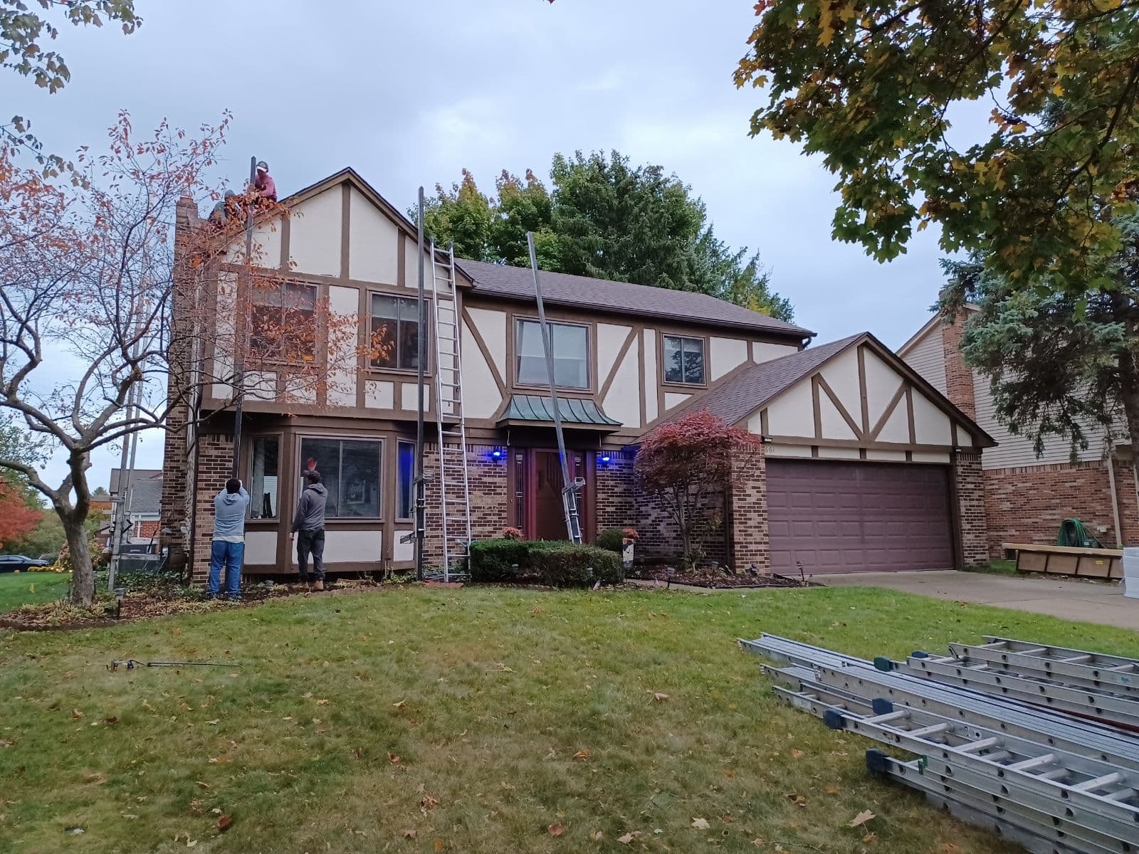 Home exterior renovation with workers installing windows during autumn. Ladders and tools nearby.