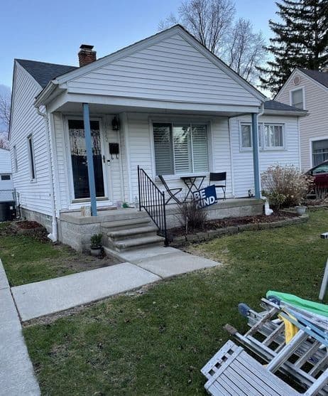 Cozy white house with a front porch, steps, and a "Be Kind" chair in the yard.