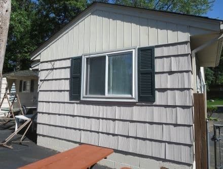 Side view of a house featuring grey siding, green window shutters, and a patio table.