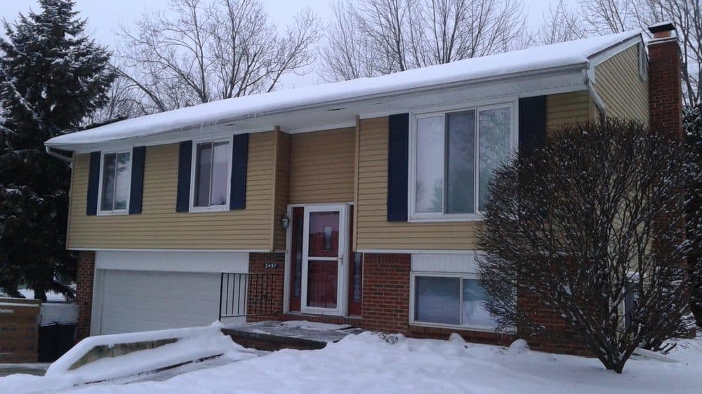 Split-level house with snow-covered yard, featuring beige siding and black shutters.