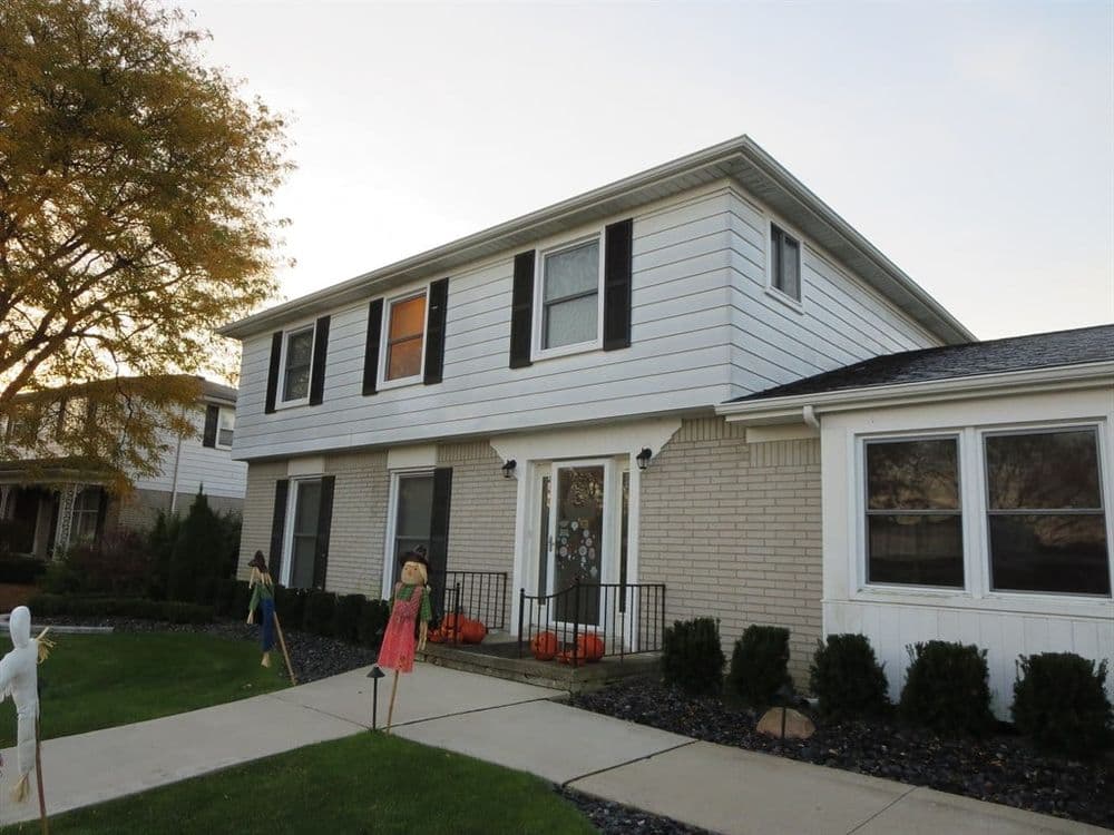 Two-story home with Halloween decorations, pumpkins on the porch, and a scarecrow in the yard.