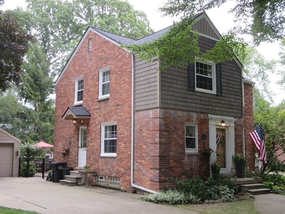 Charming brick house with American flag, trees, and landscaped yard in suburban neighborhood.