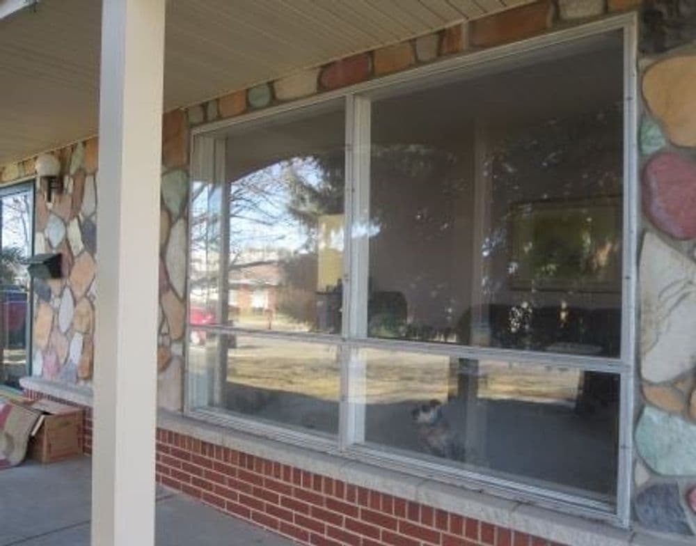 Front porch with large windows showcasing a stone exterior and a view of the lawn.