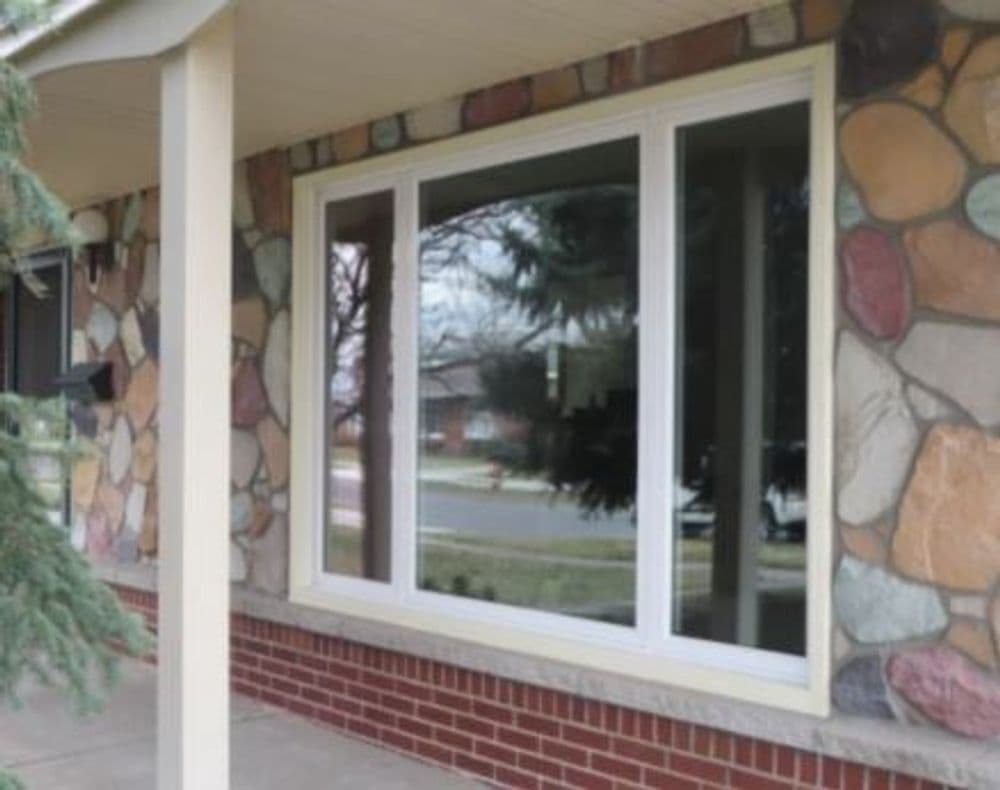 Modern large window on a brick and stone exterior of a home with a landscaped view.