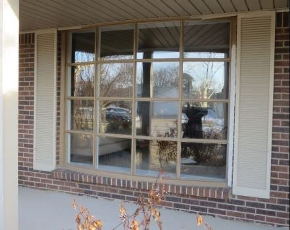 Traditional house window with divided panes and shutters, showcasing a brick exterior.
