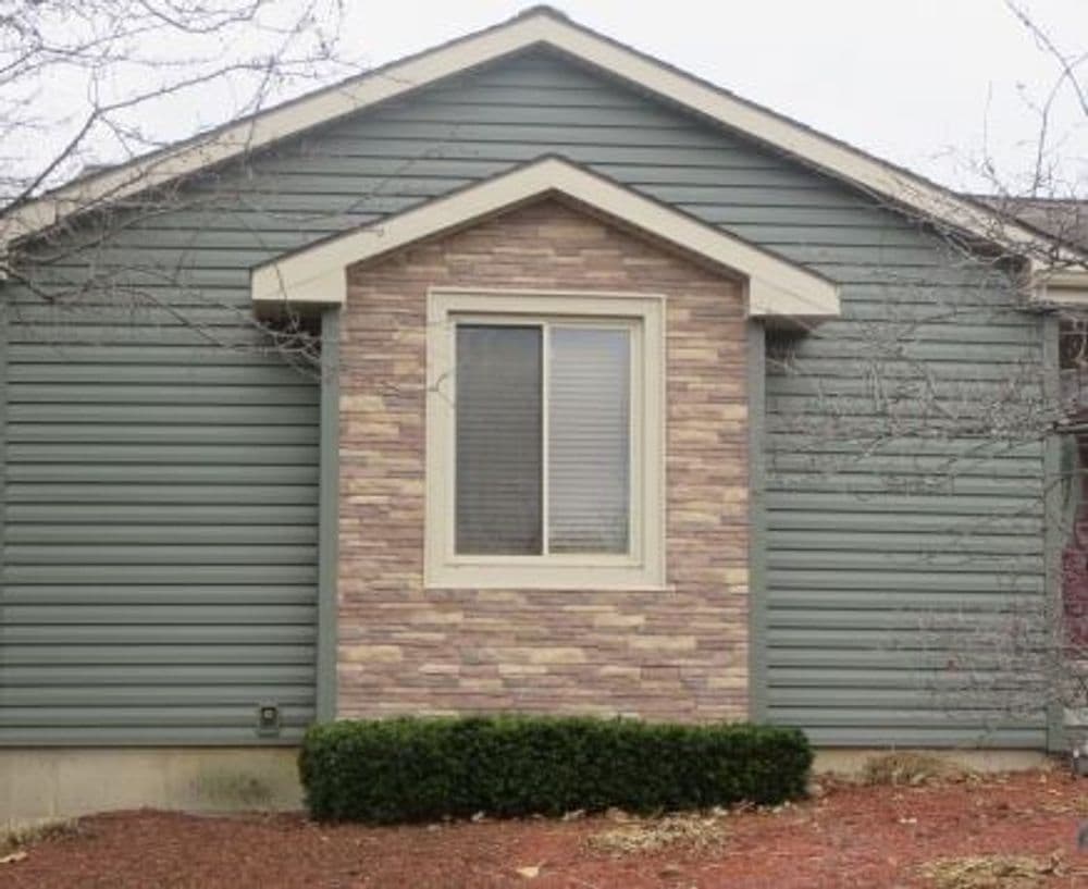 Exterior view of a green house featuring stone accent and a front window.