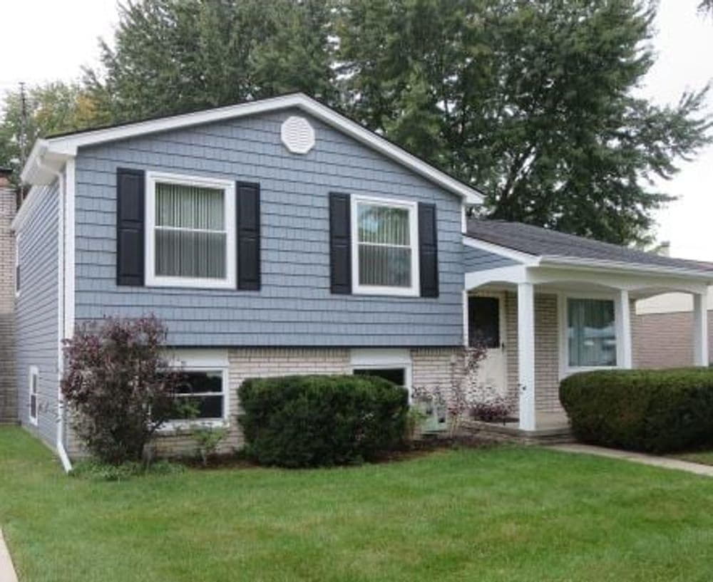 Two-story blue house with white trim, black shutters, and well-maintained landscaping.