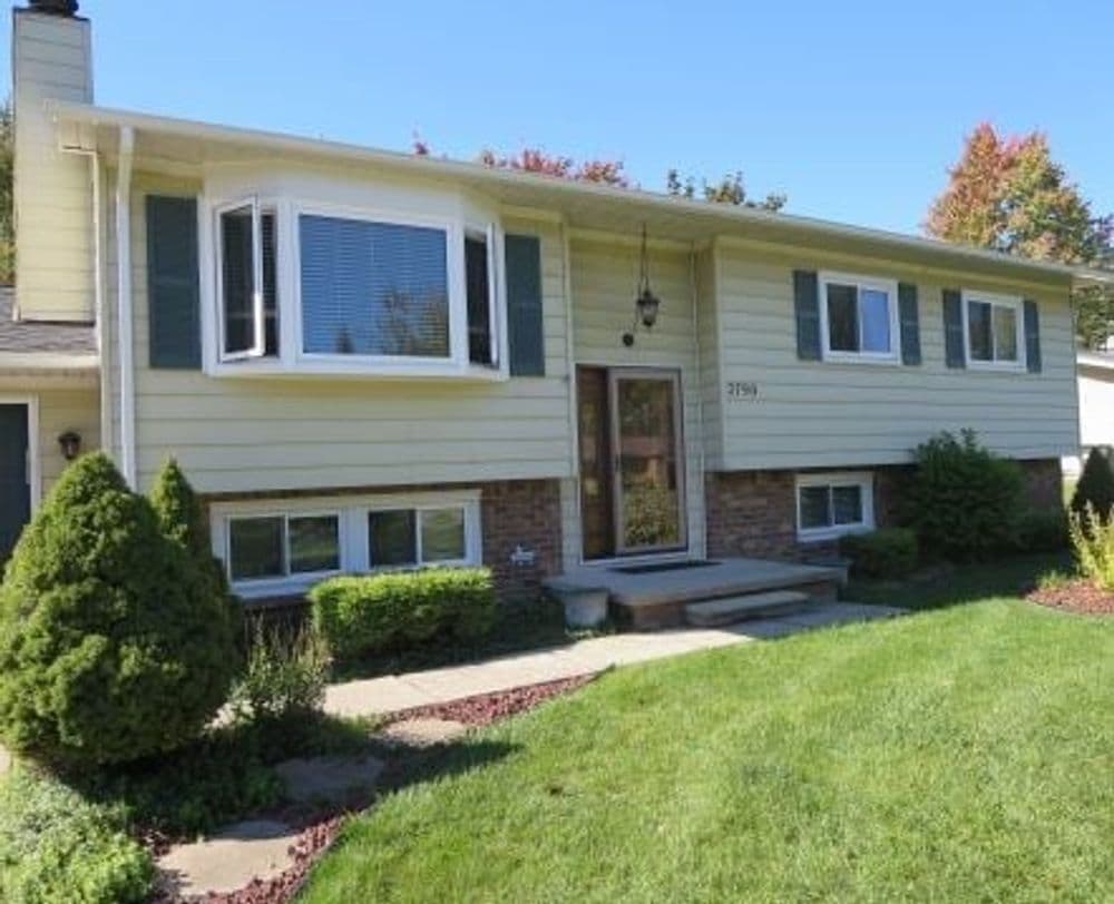 Two-story suburban home with a front yard, large windows, and lush greenery.