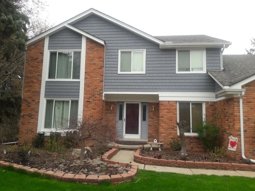 Two-story brick and gray vinyl siding house with landscaped front yard and pathway.